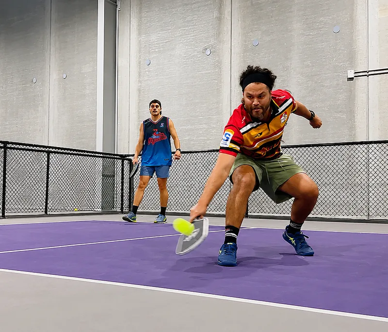 Player reaching for a pickleball on the indoor courts